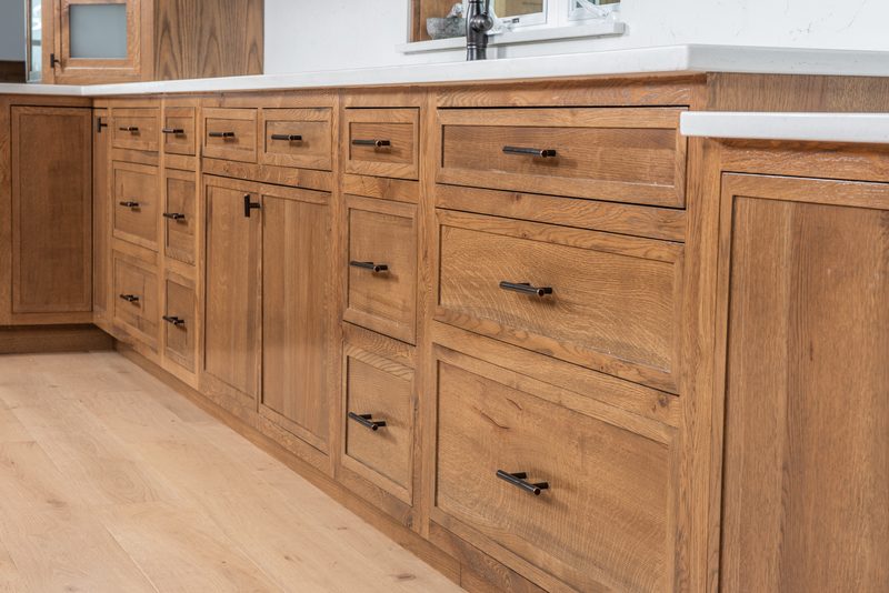 A run of oak base cabinets with inset drawer fronts and black pulls