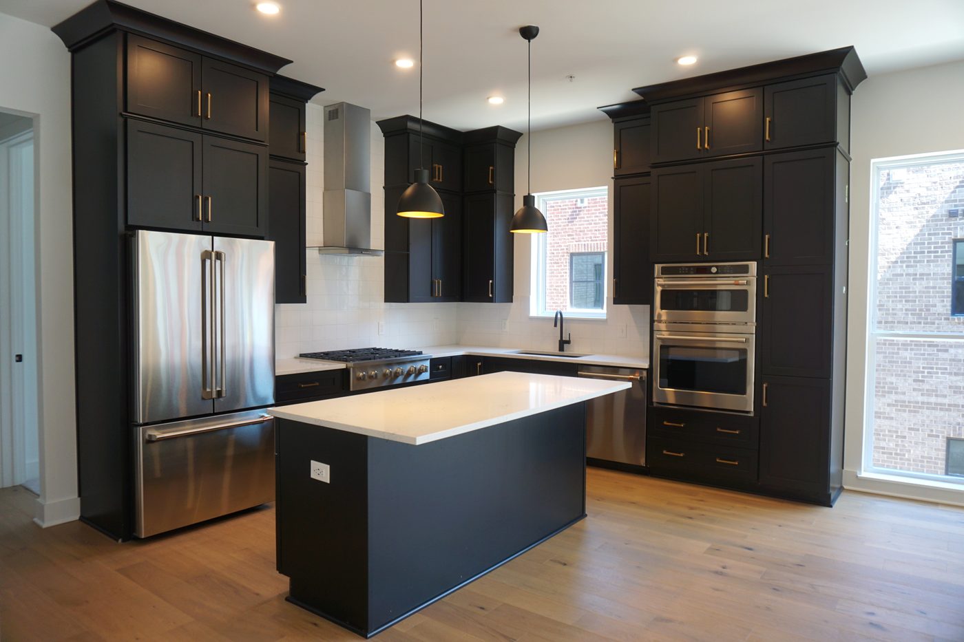 A kitchen in dark painted cabinetry with a center island, brass pulls and stainless appliances